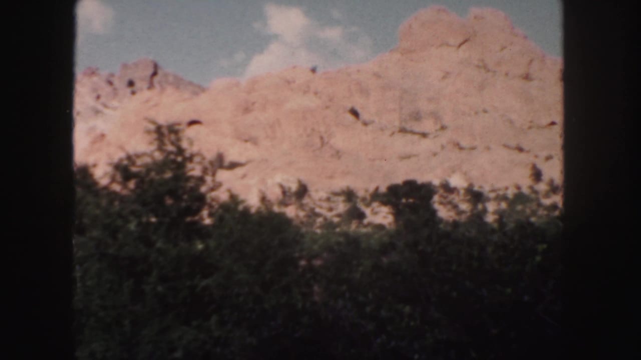 Rocky ridge with dark trees in the foreground and clouds overhead.