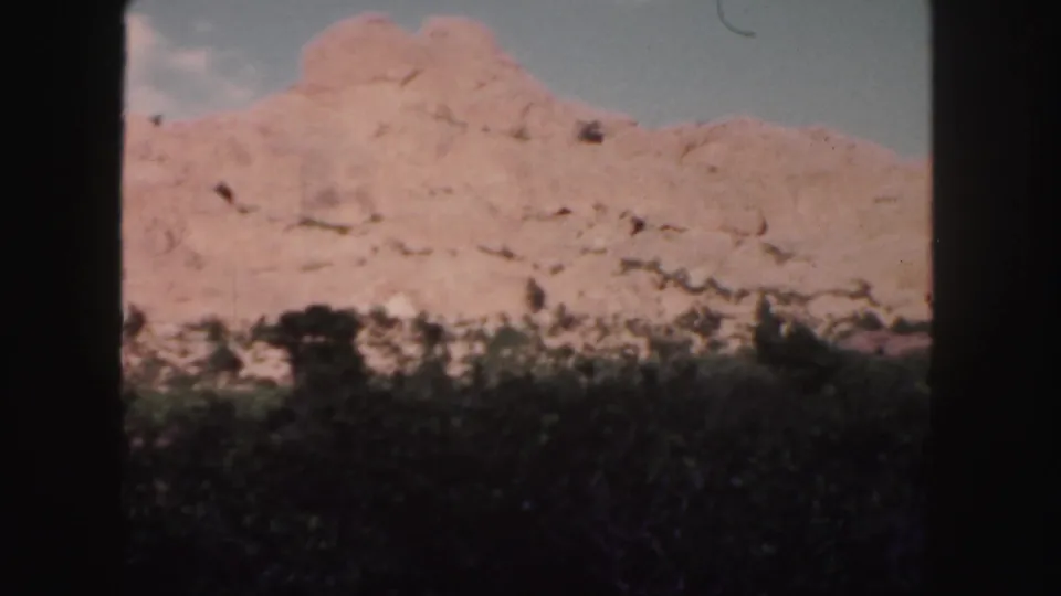 Colorado 8mm still showing a reddish mountain slope, dark vegetation, and pale clouds within a soft home-movie frame.