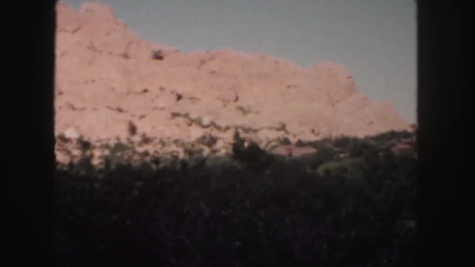 Red rock formations in Colorado fill the upper frame, with dark vegetation below and visible 8mm gate edges.