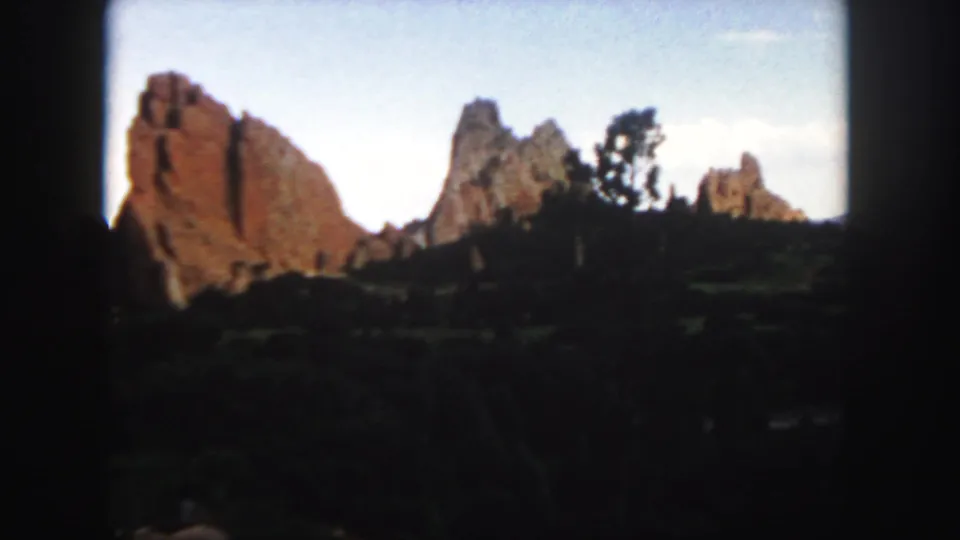 A handheld 8mm view of Colorado red rock formations with trees and shadowed vegetation in the foreground.