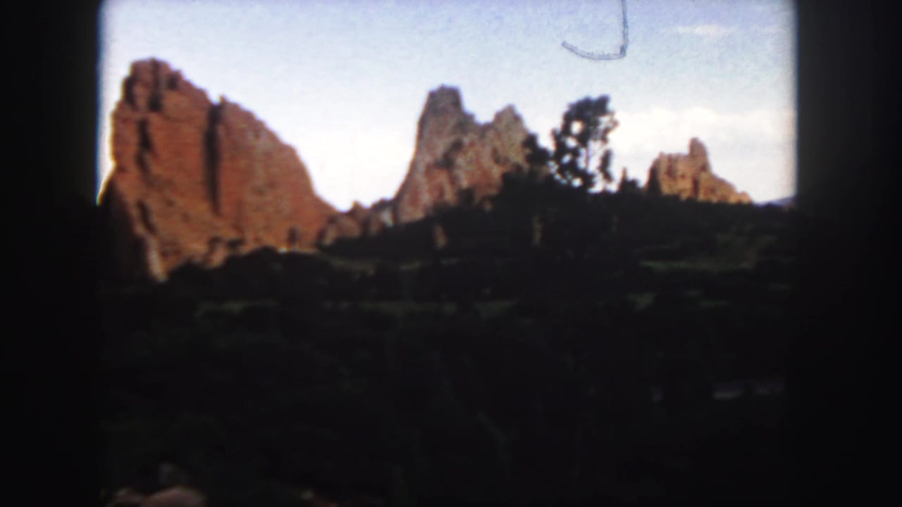 1958 Colorado 8mm frame showing red sandstone formations beyond shadowed vegetation and a pale blue sky.