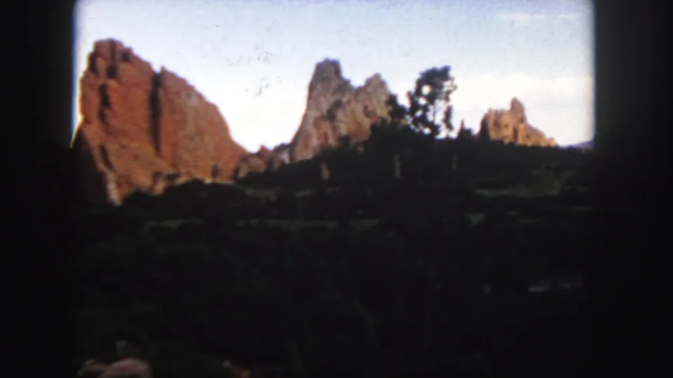 Home-movie view of Colorado red rocks with shadowed brush in front and soft-focus formations against the sky.