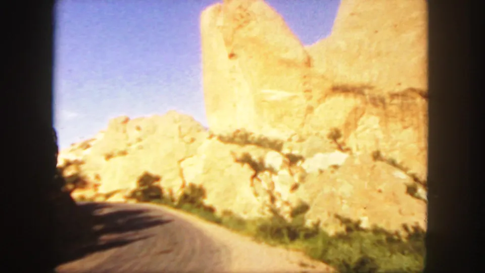 A curving road or path passes below pale sandstone formations in Colorado, with vegetation along the edge.