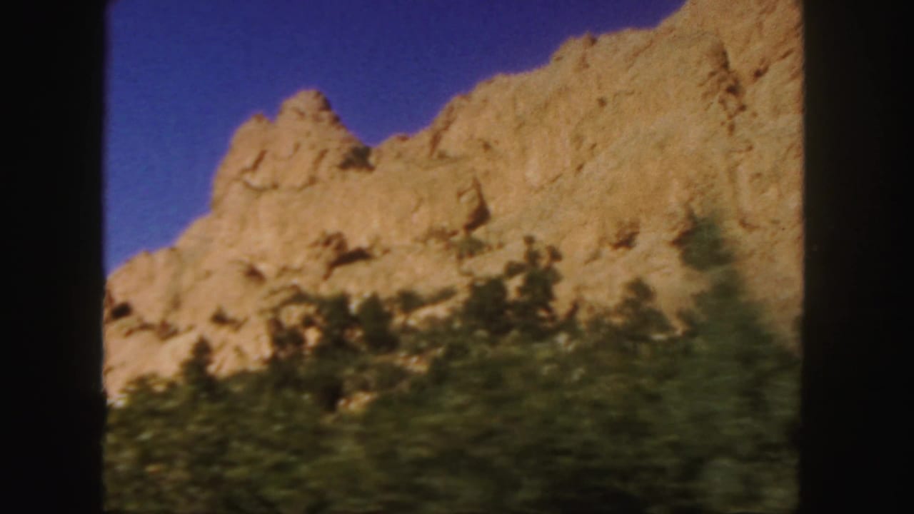 Rocky tan slope and blurred green vegetation seen through black film-frame borders.