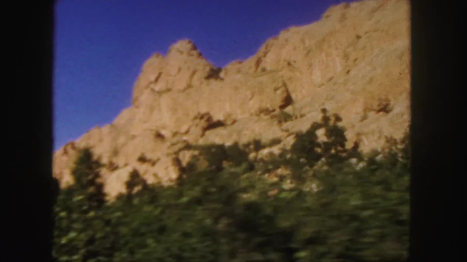 1958 Colorado 8mm frame with a tan rock outcrop above dark roadside vegetation, filmed from a moving car.