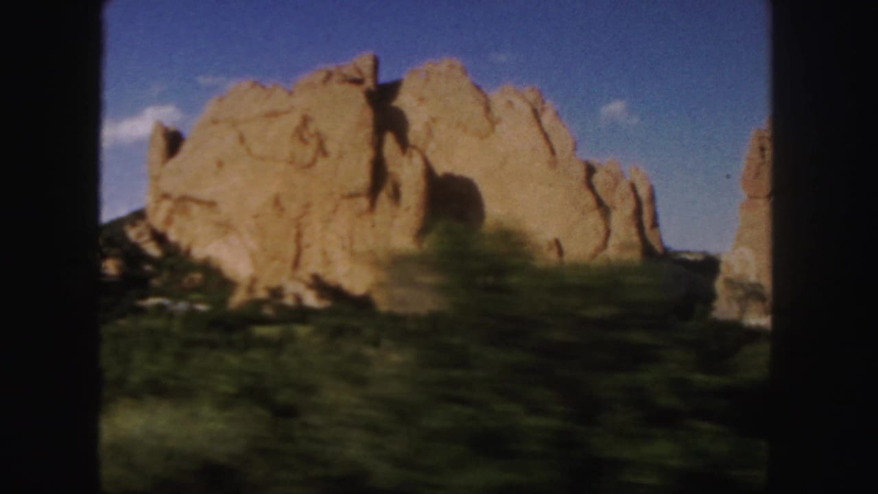 Large sandstone outcrop seen past dark film-frame borders and blurred vegetation.