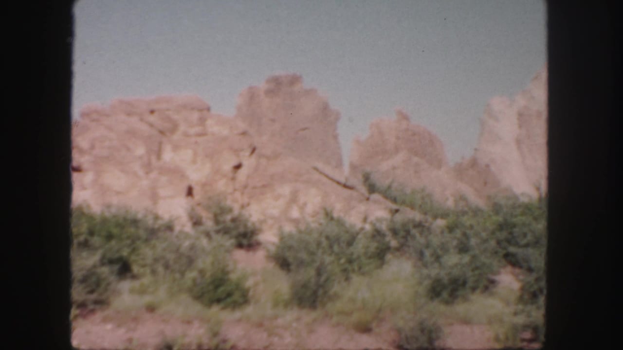 Rocky outcrops and desert shrubs framed by dark film borders.