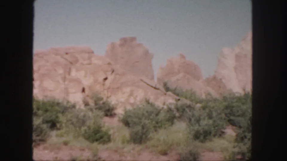 Vintage 8mm Colorado landscape frame with tall sandstone shapes behind scrub and dry soil.