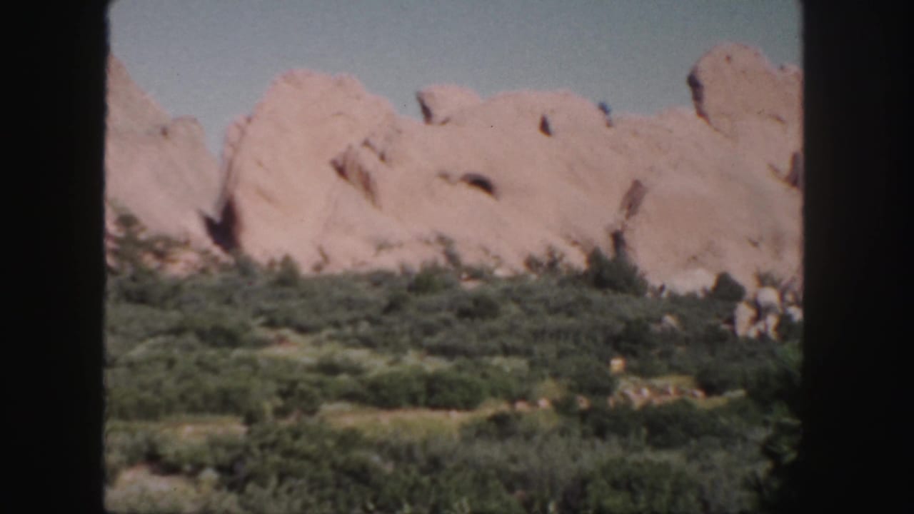 Pink rock formations above green scrub under a blue sky, framed by dark 8mm film edges.