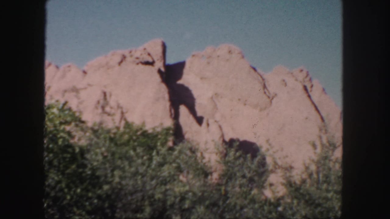 Jagged tan rock formation with shrubs across the lower frame.