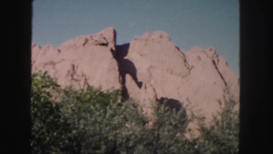 1958 Colorado home-movie view of a jagged tan rock formation, partly shadowed, with shrubs filling the foreground.