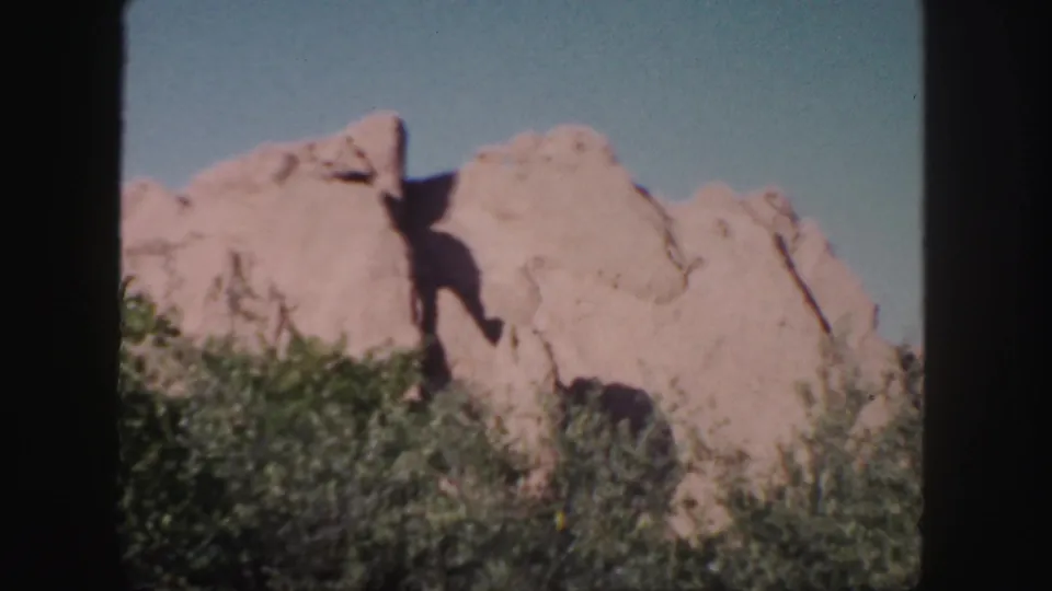 1958 Colorado 8mm still with pale tan rock, leafy green foreground growth, and a clear sky in bright daylight.