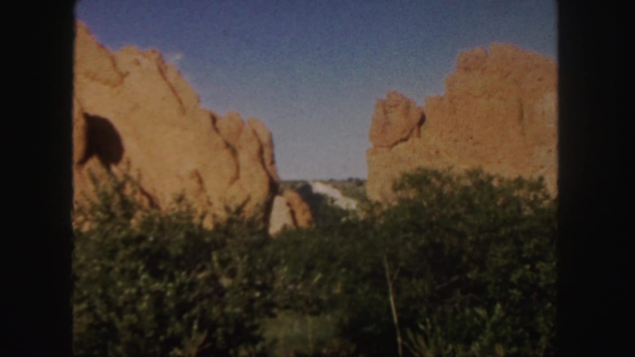 Red sandstone formations rise above dark green undergrowth beneath a blue sky.