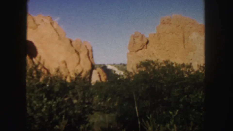 1958 Colorado 8mm frame showing sunlit red rock, darker foreground vegetation, and blue sky with soft handheld framing.