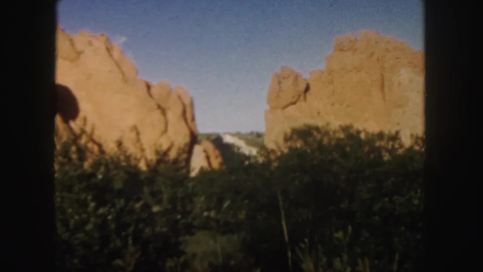 Final 1958 Colorado frame with red sandstone masses, green undergrowth, and a clear sky in grainy color 8mm footage.