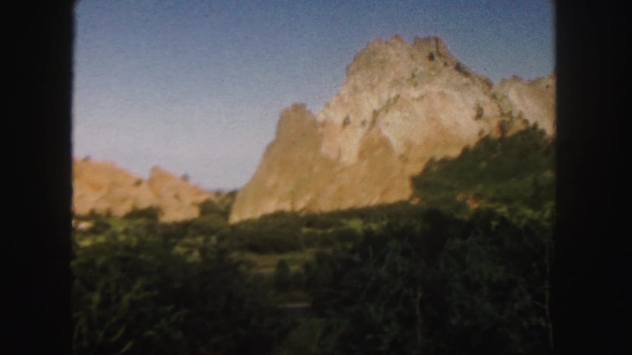 Large sandstone formation with green brush in the foreground and blue sky above.