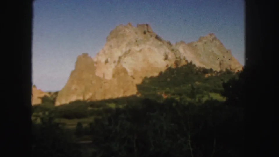 1958 Colorado 8mm view of sunlit red rock ridges, shadowed shrubs, blue sky, and rounded film-frame edges.