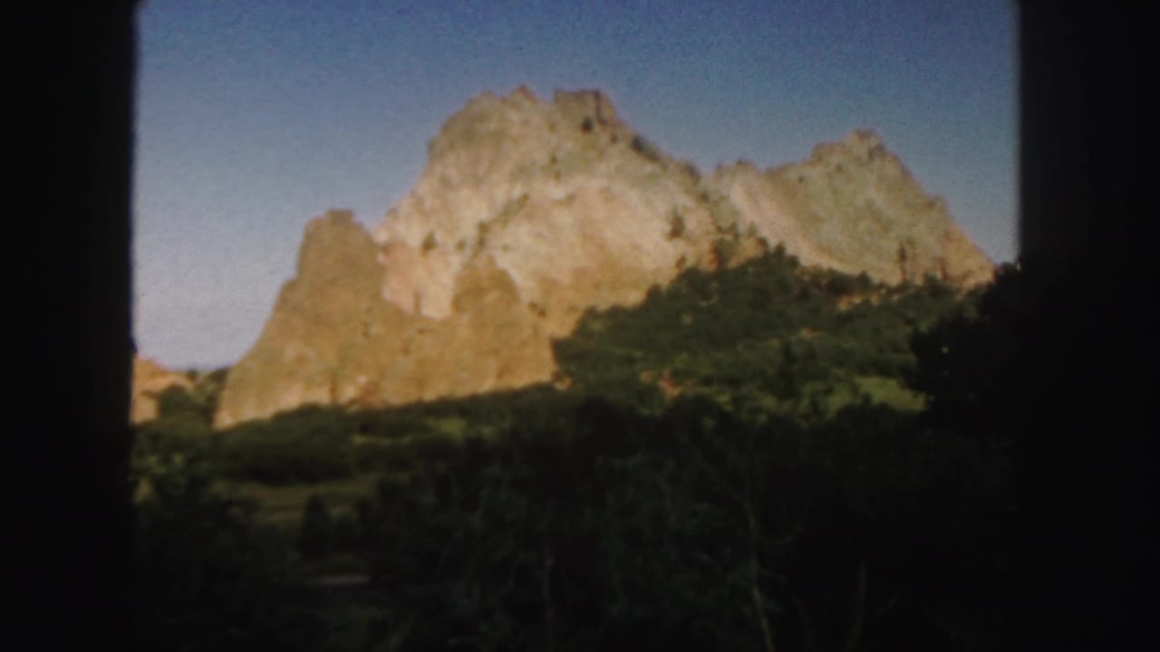 1958 Colorado 8mm frame showing a sunlit sandstone rock formation rising above shaded trees beneath a clear blue sky.