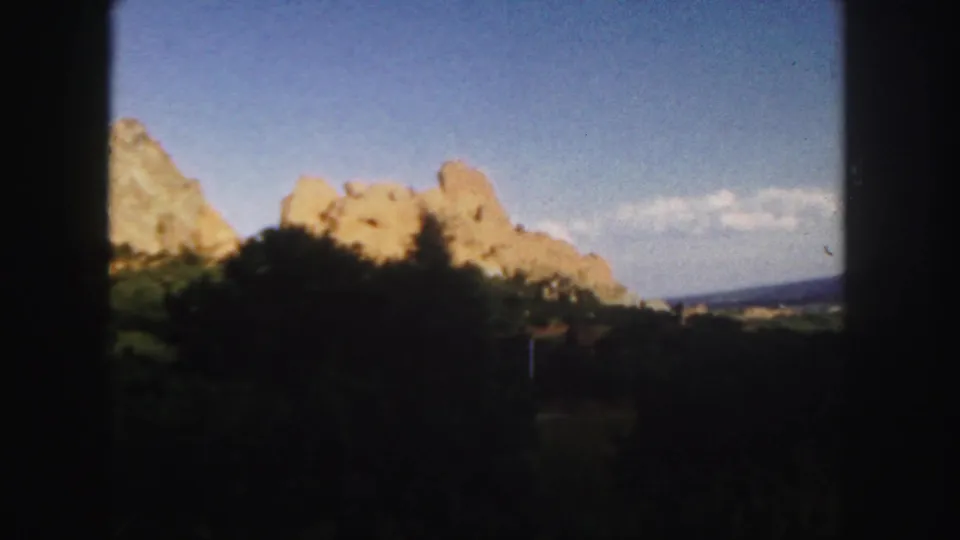 1958 Colorado 8mm frame showing part of the rock formation, shaded vegetation, and blue sky in a visitor-shot landscape view.
