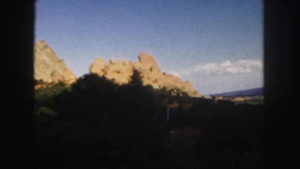 1958 Colorado 8mm frame of a sunlit sandstone ridge above dark foreground trees, framed by visible contact-sheet borders.