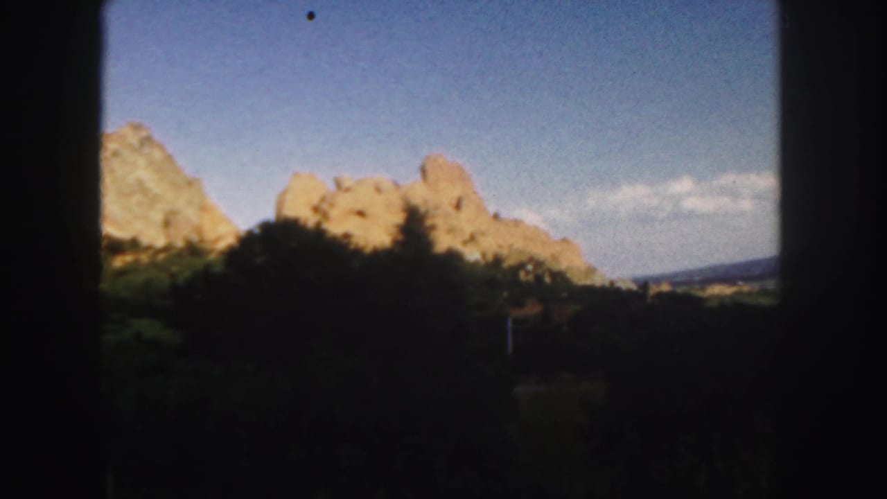 1958 Colorado 8mm frame showing sunlit rocky formations, dark vegetation, and a blue sky within heavy gate framing.