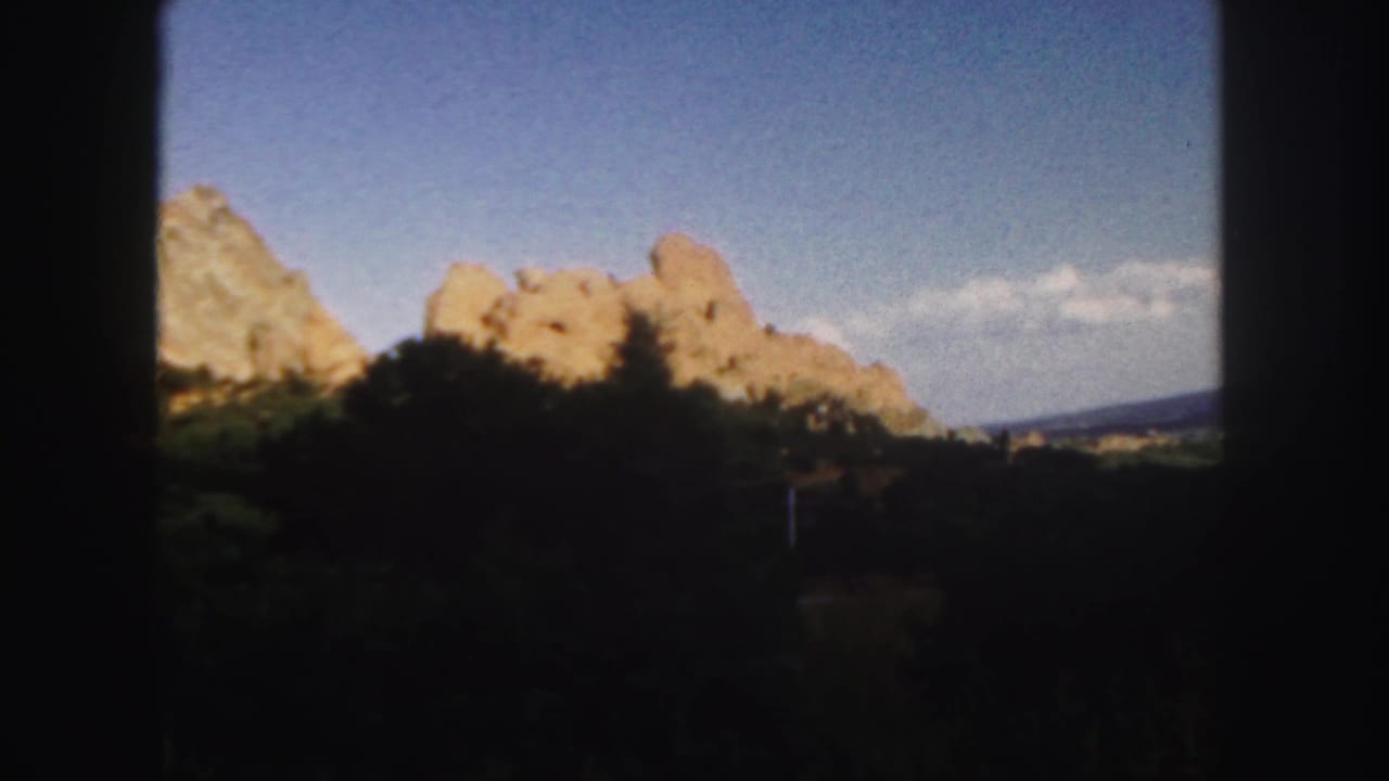 Sunlit rocky formations and dark vegetation seen through a heavy black frame.