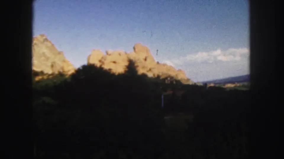 A 1958 Colorado home-movie frame shows rocky terrain and dark foreground brush within visible 8mm frame borders.