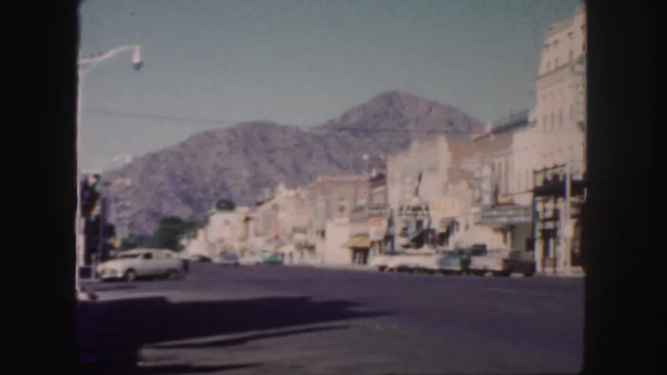 1958 Colorado town view with parked cars, storefront awnings, hotel signage, a broad road, and mountains visible beyond the commercial block.