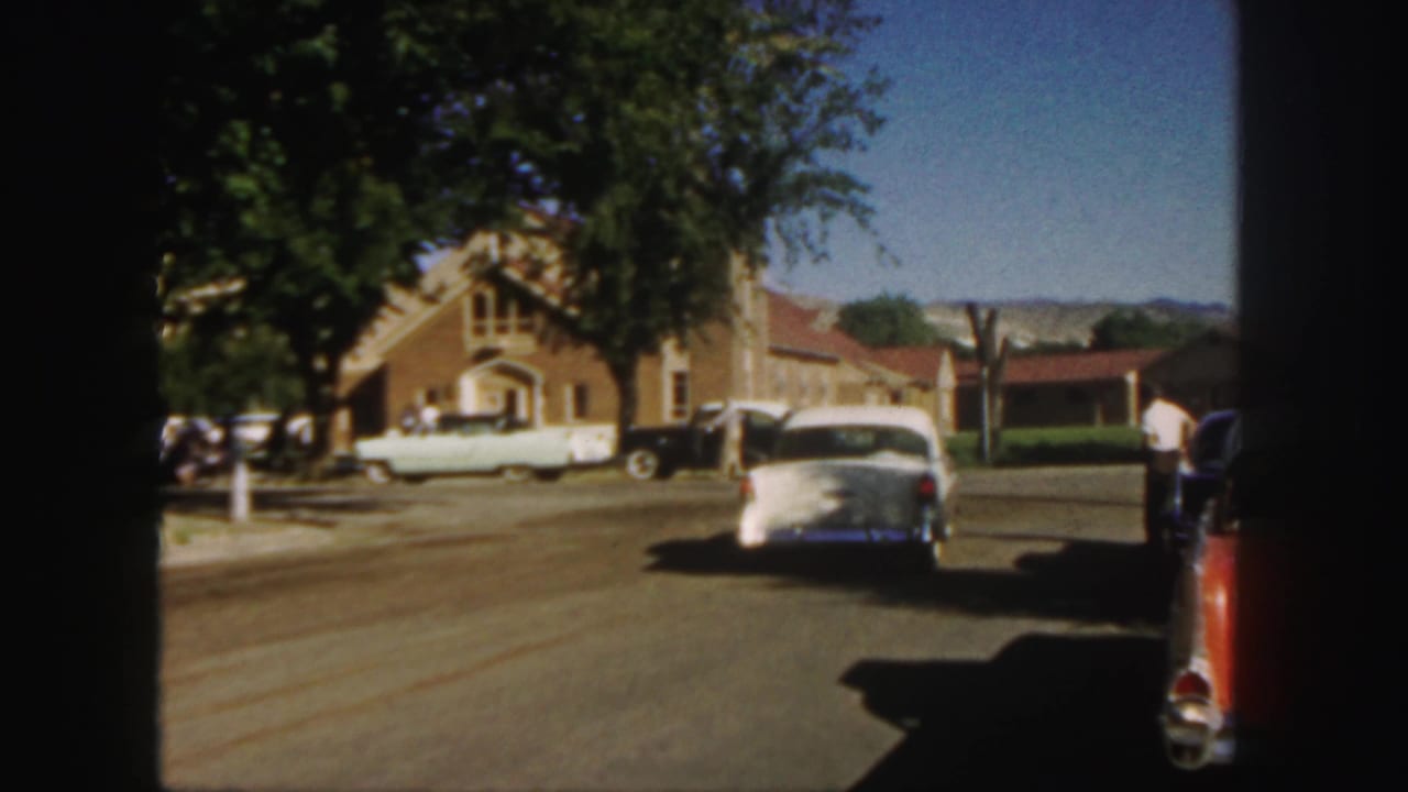 White sedan farther down the road near a brick church, trees, and parked cars.