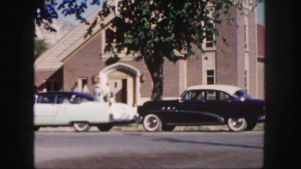1958 Colorado 8mm view of parked mid-century cars outside a brick church entrance, with people standing near the doorway.