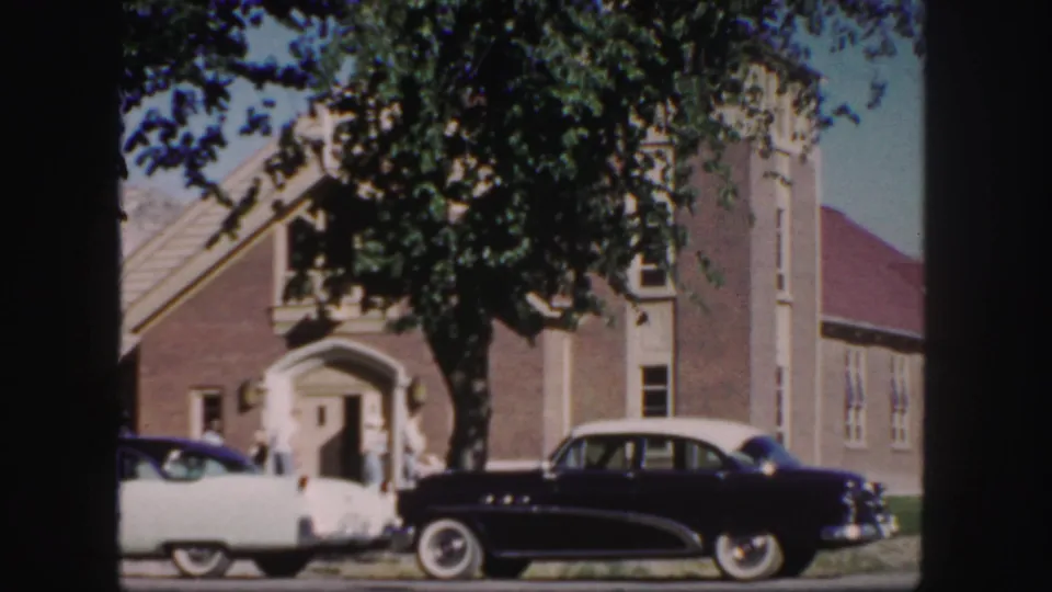 1958 Colorado 8mm frame showing a brick church exterior, parked mid-century cars, and people near the arched entrance.