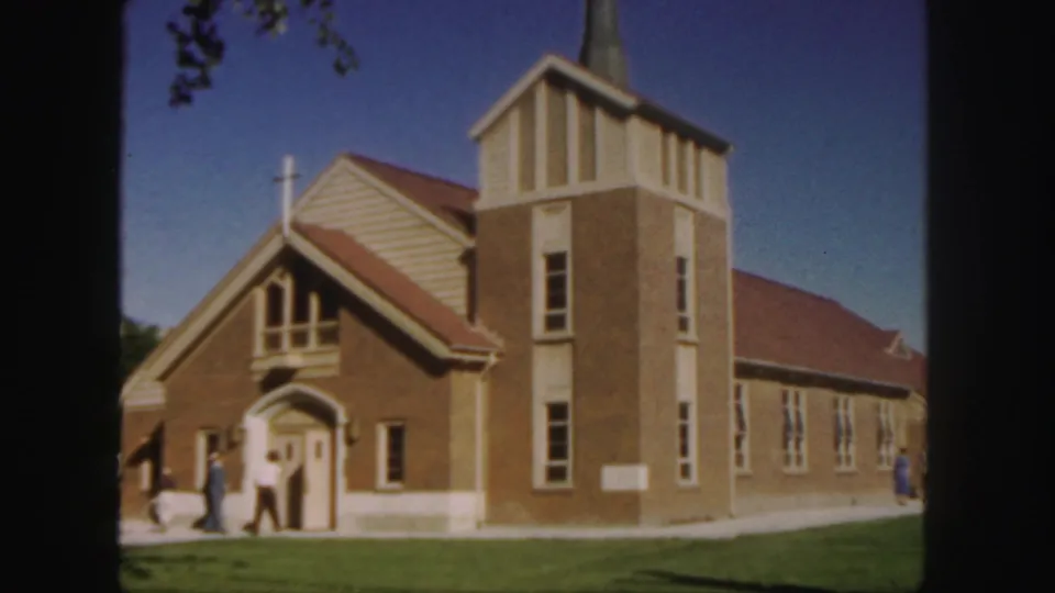 Wider 1958 Colorado view of the brick church, showing its tower, steeple, lawn, sidewalk, and people outside.