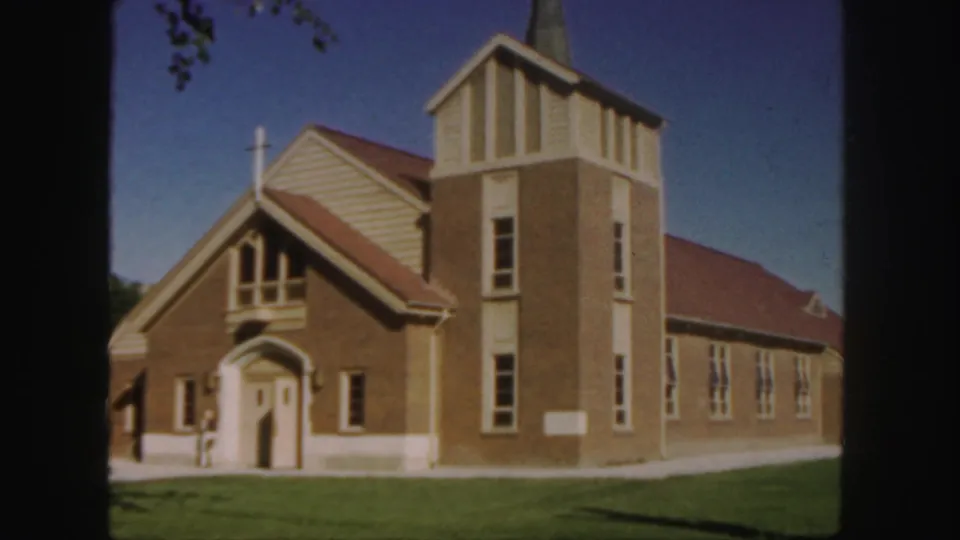 1958 Colorado 8mm frame with a closer view of the brick church entrance, steeple, red roof, tall windows, and lawn.