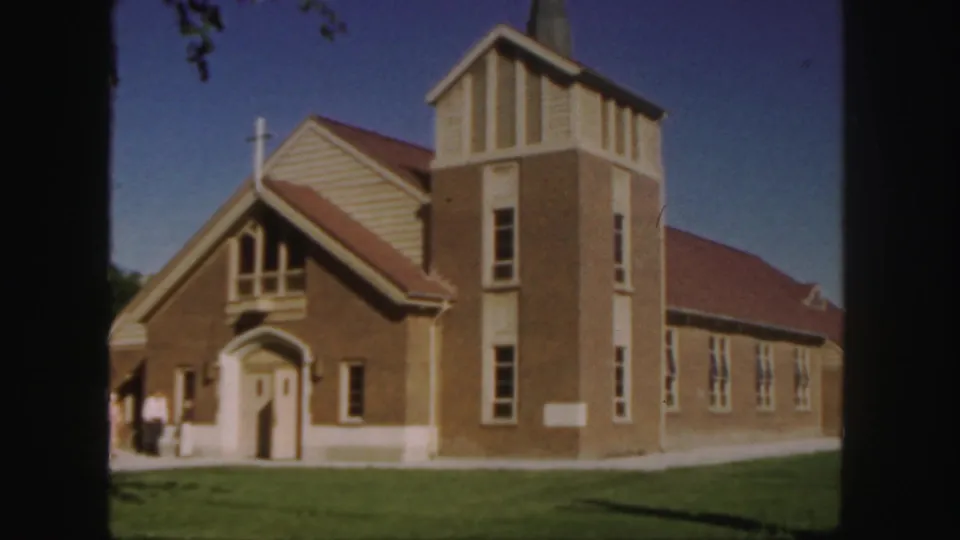 1958 Colorado home-movie frame of the same church from a similar angle, with people gathered near the arched entrance.