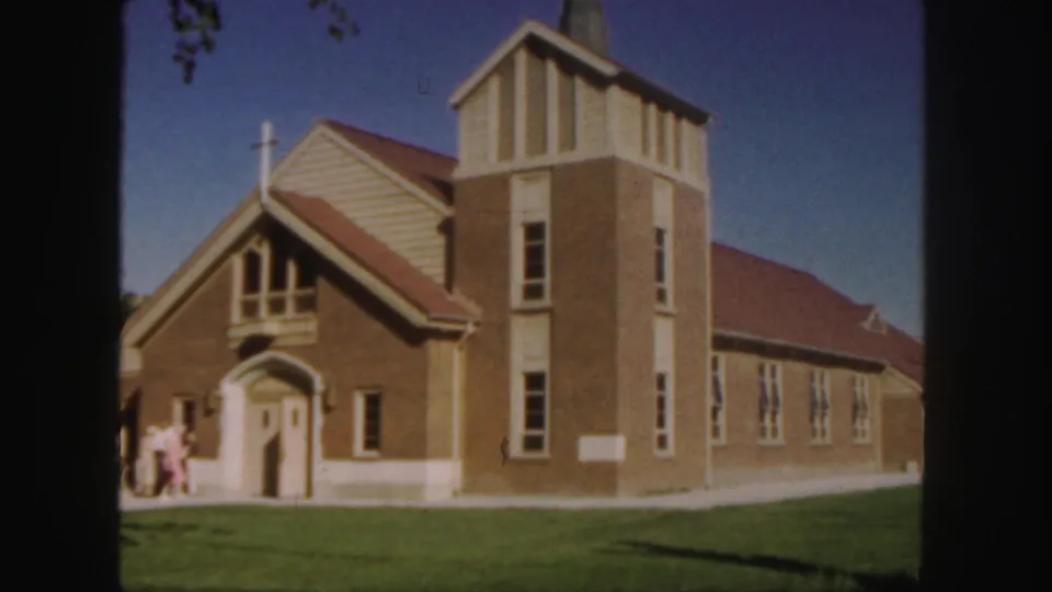1958 Colorado 8mm frame with a closer view of the church facade, arched doorway, steeple tower, and people at the entrance.