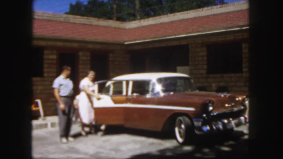 The woman opens the door of the two-tone station wagon while the man stands near her outside the Colorado motel.