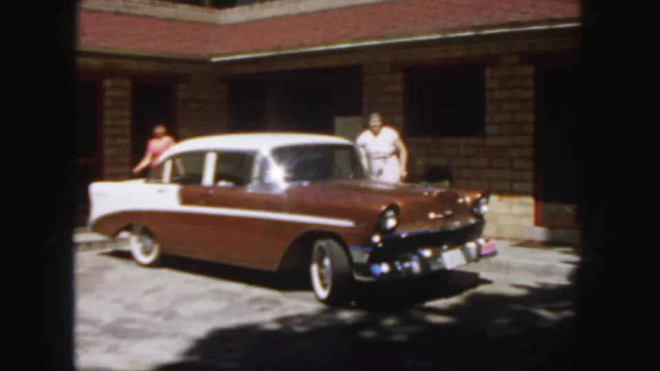 1958 Colorado frame showing the brown and white sedan with one adult in white near the front and another in red partly visible at the rear.