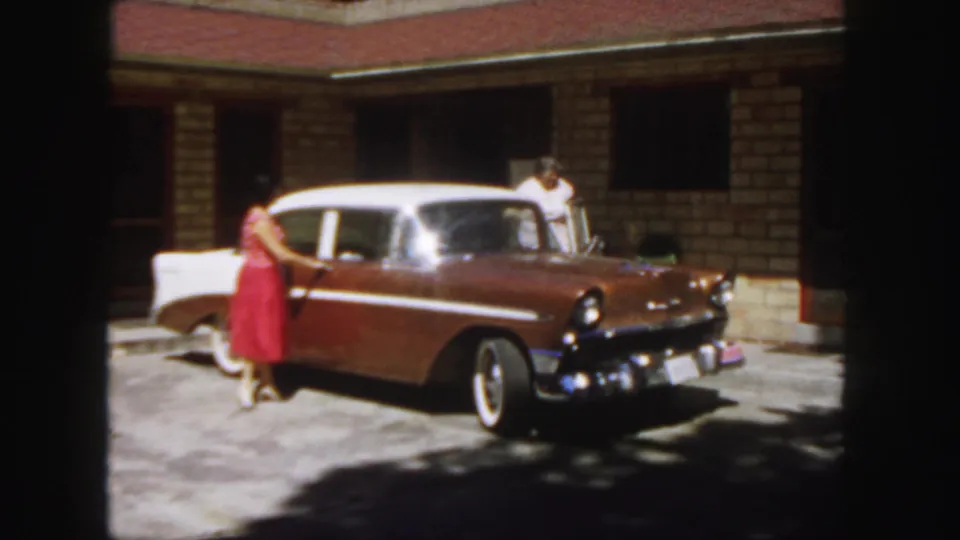 1958 Colorado frame with a woman in a red dress opening a sedan door while another woman stands near the house.