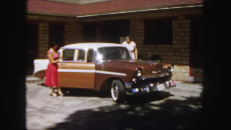1958 Colorado home-movie frame showing a woman beside the sedan door, with another woman behind the car.