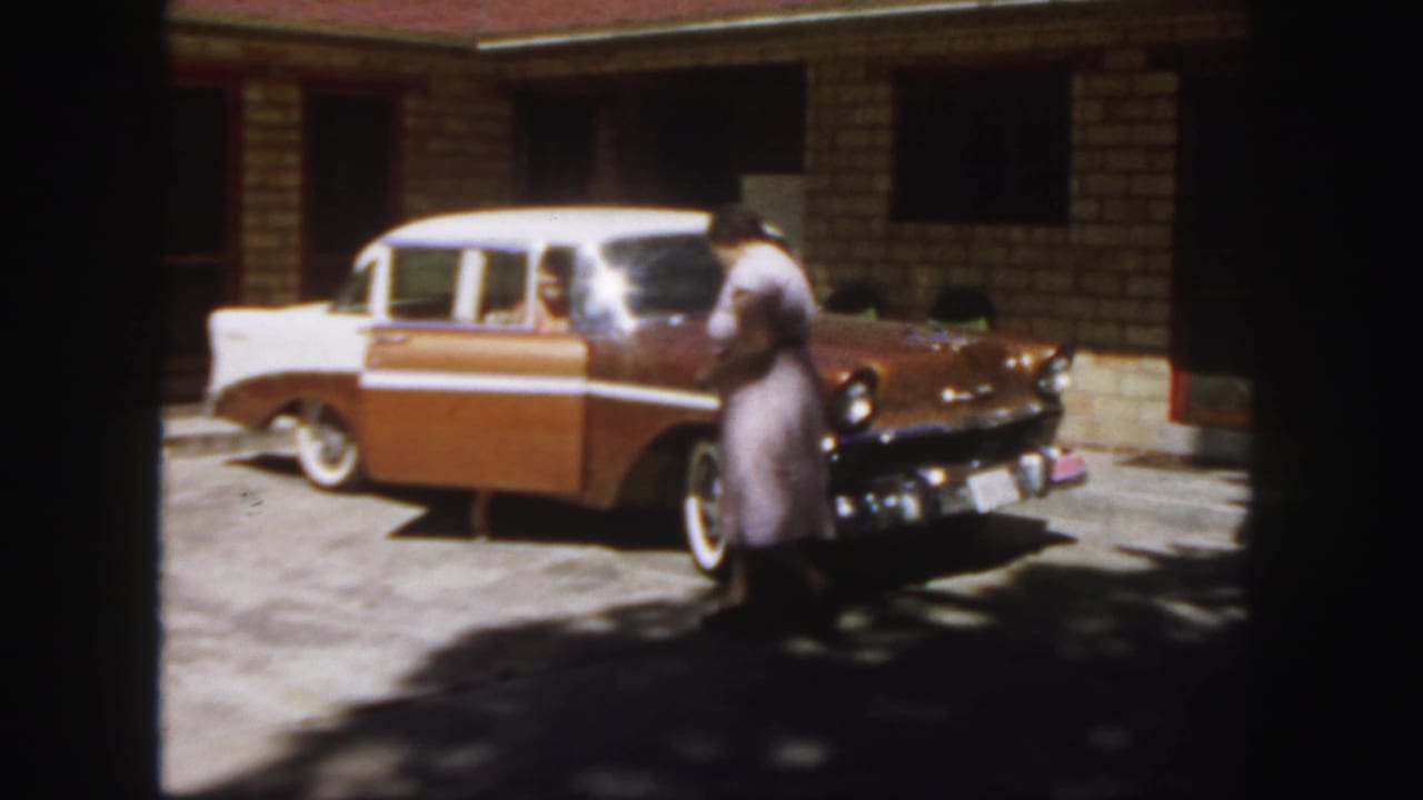 Woman walks past the front of the brown and white sedan while the rear passenger door stays open.