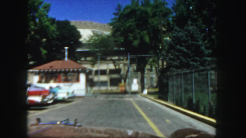 Final frame shows the Colorado State Penitentiary entrance approach, including the small booth, fence line, road, cars, trees, and hillside.