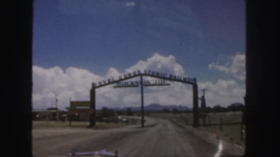 1958 home-movie frame showing the Royal Gorge Scenic Railway entrance sign over a dirt road in Colorado.