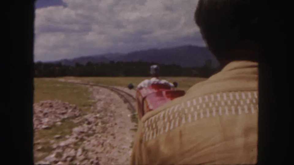 Passenger perspective on a Colorado scenic railway, showing the back of a man and the train ahead crossing grassland toward distant hills.