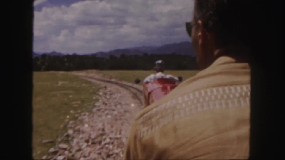 Colorado scenic railway footage from 1958, with a seated man in the foreground and the train moving along a curve under a cloudy sky.