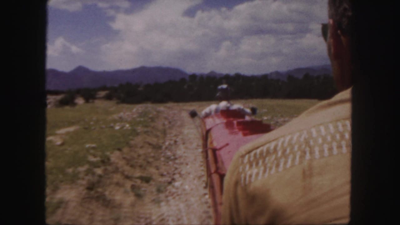 Rider's view from a red miniature train on a dirt track with mountains ahead.