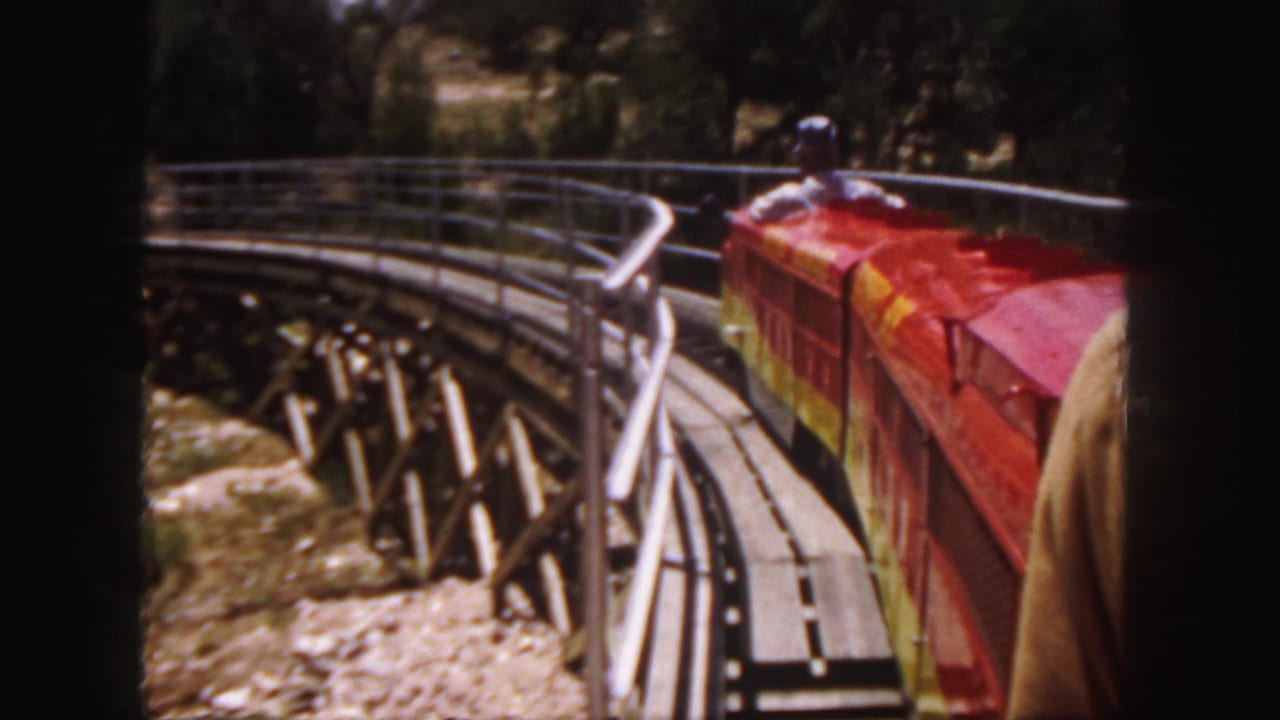 1958 Colorado 8mm frame showing a red miniature train rounding a curved trestle from a passenger viewpoint.