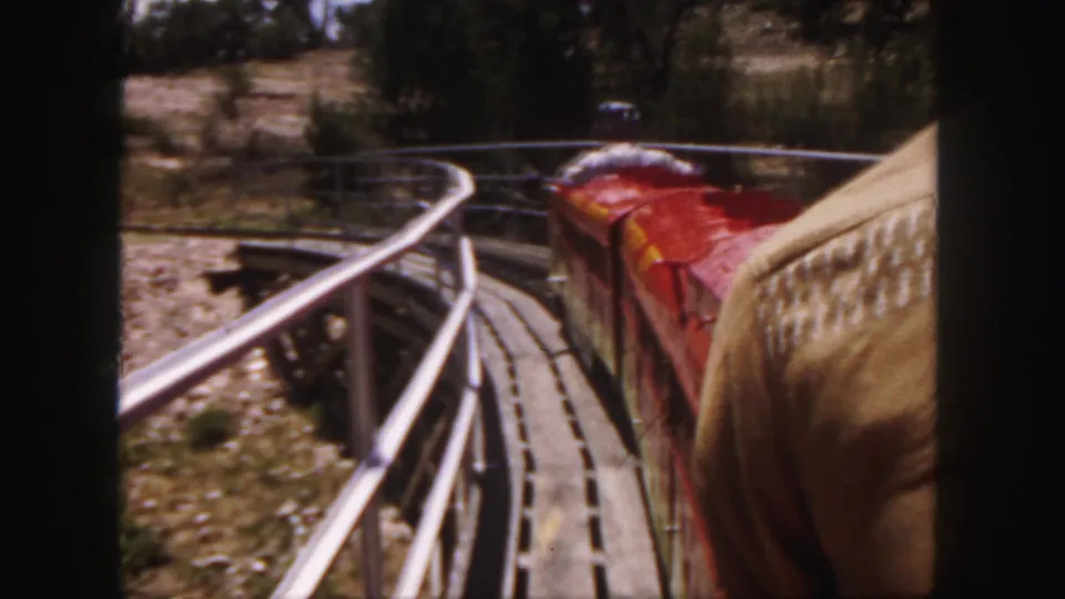 Close passenger-side view of the red miniature train on a curved trestle in 1958 Colorado home-movie footage.