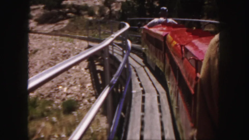 Passenger-perspective 1958 Colorado frame of a red miniature train continuing along a curved wooden trestle.