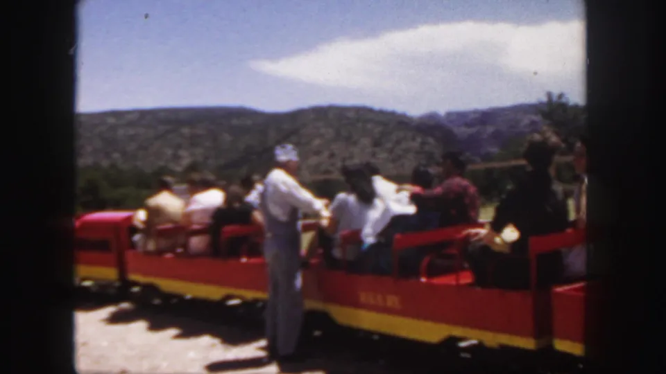 Color 8mm frame from Colorado in 1958 showing a visitor train with passengers, sunlit ground, and rolling hills beyond.