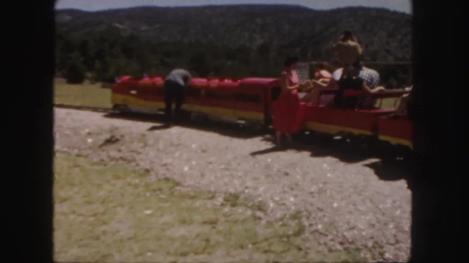 Final frame shows the red and yellow tour train on gravel with seated visitors, a person bending near the cars, and wooded Colorado hills beyond.